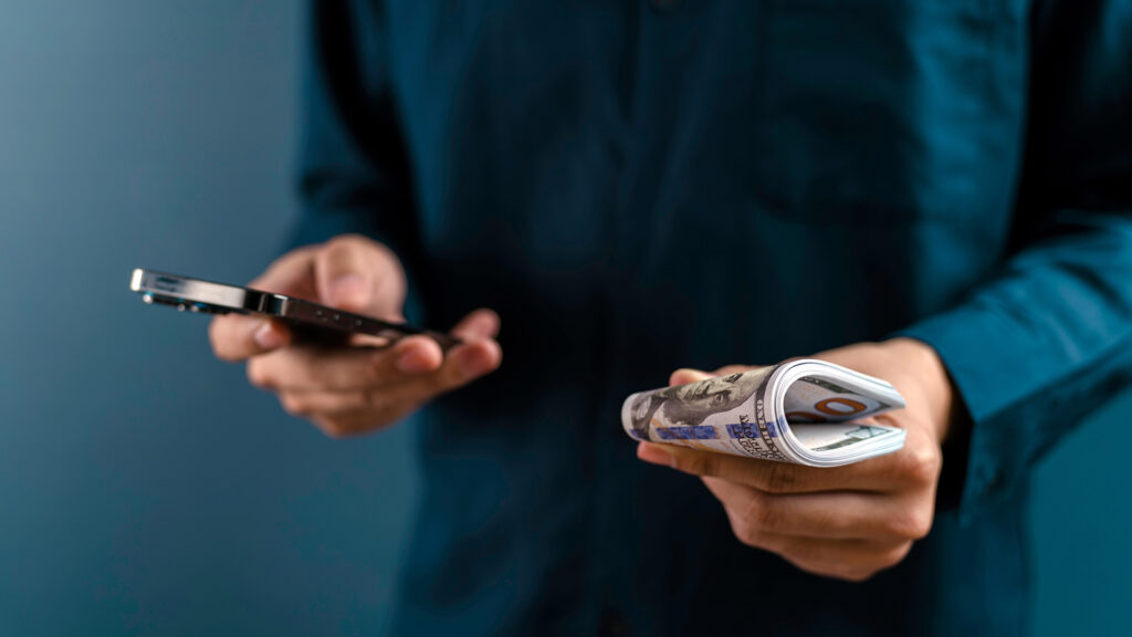 Person with a mobile phone in one hand and cash in the other