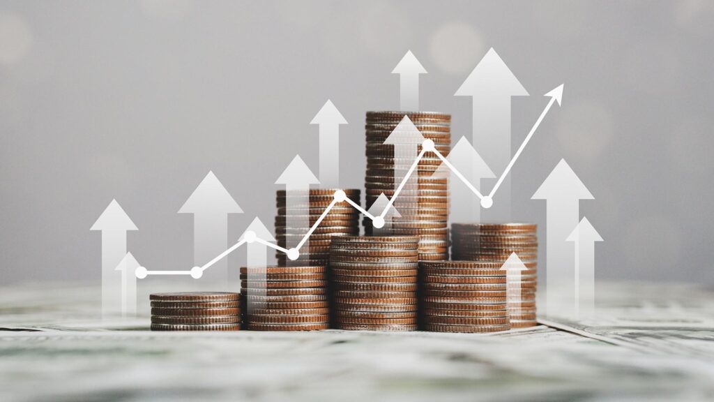 Stacks of coins on top of notes with arrows and charts going up