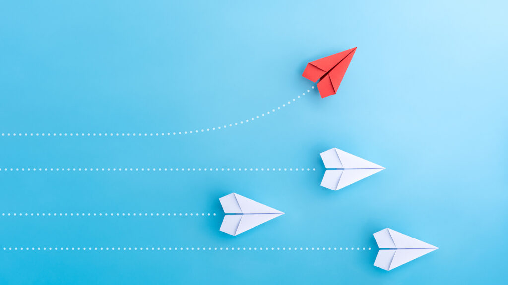 Group of white paper planes flying in one direction with one single red plane flying away